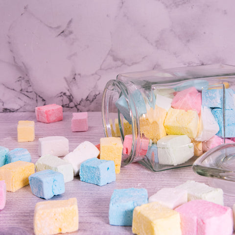 Different coloured and flavoured marshmallows on a surface spilling out of a glass jar