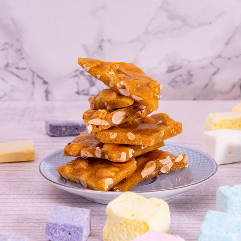 Brittle pieces placed into a pile onto a plate with marshmallows and crunchy hard marshmallows spread around it 